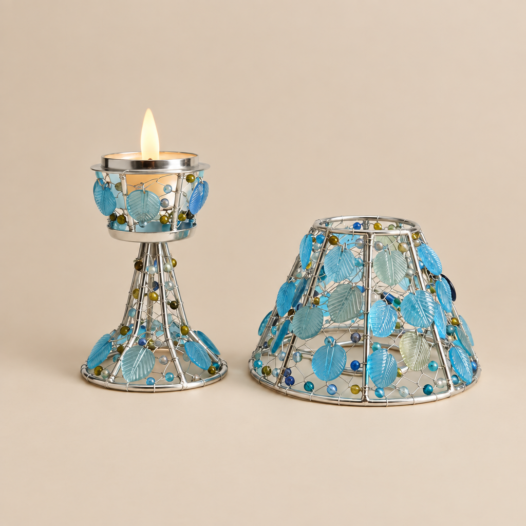 A decorative silver metal candle holder with blue seashell and bead embellishments, shown with a lit candle in one piece and the matching shade removed beside it on a light gray background.