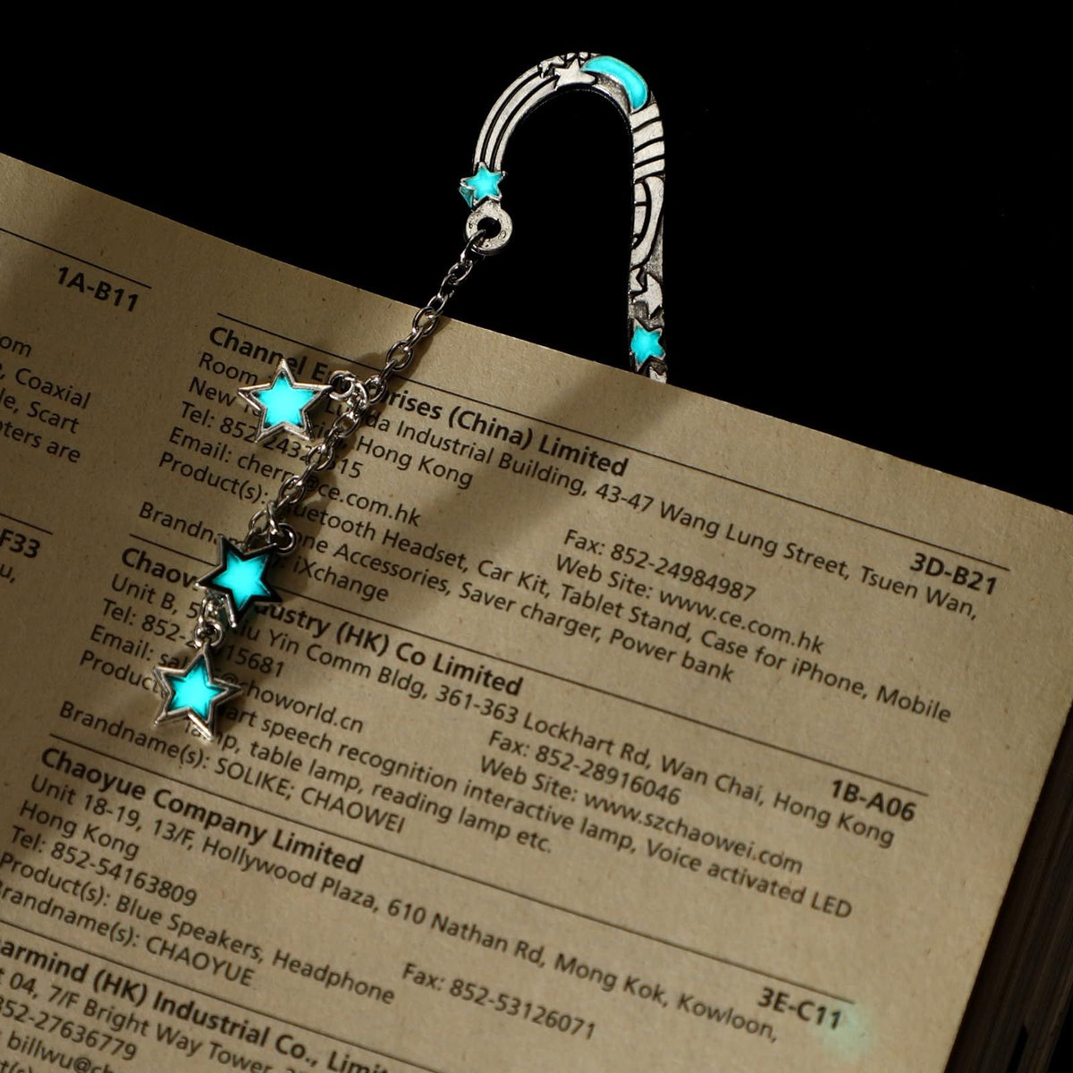 A silver-toned metal car accessory set featuring a curved hook clip, a short chain, and three dangling star charms, each embellished with a small turquoise blue star. The charms are displayed resting on top of a printed paper document against a solid black background.
