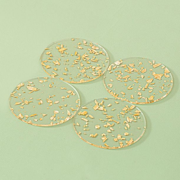 Four round clear resin coasters with embedded gold foil flakes, arranged on a solid pale green background.