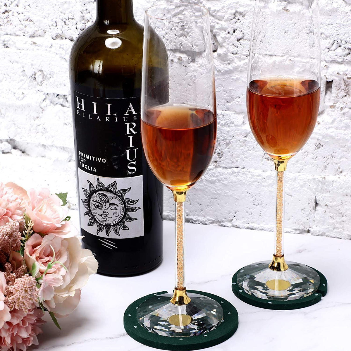 Wine bottle labeled 'Hilararius' with two glasses of red wine on a white surface with flowers.
